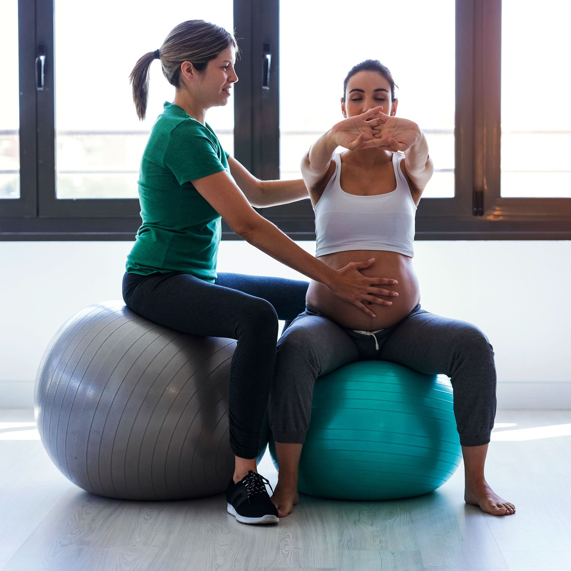 Zwangere vrouw doet een oefening op een fitnessbal onder begeleiding